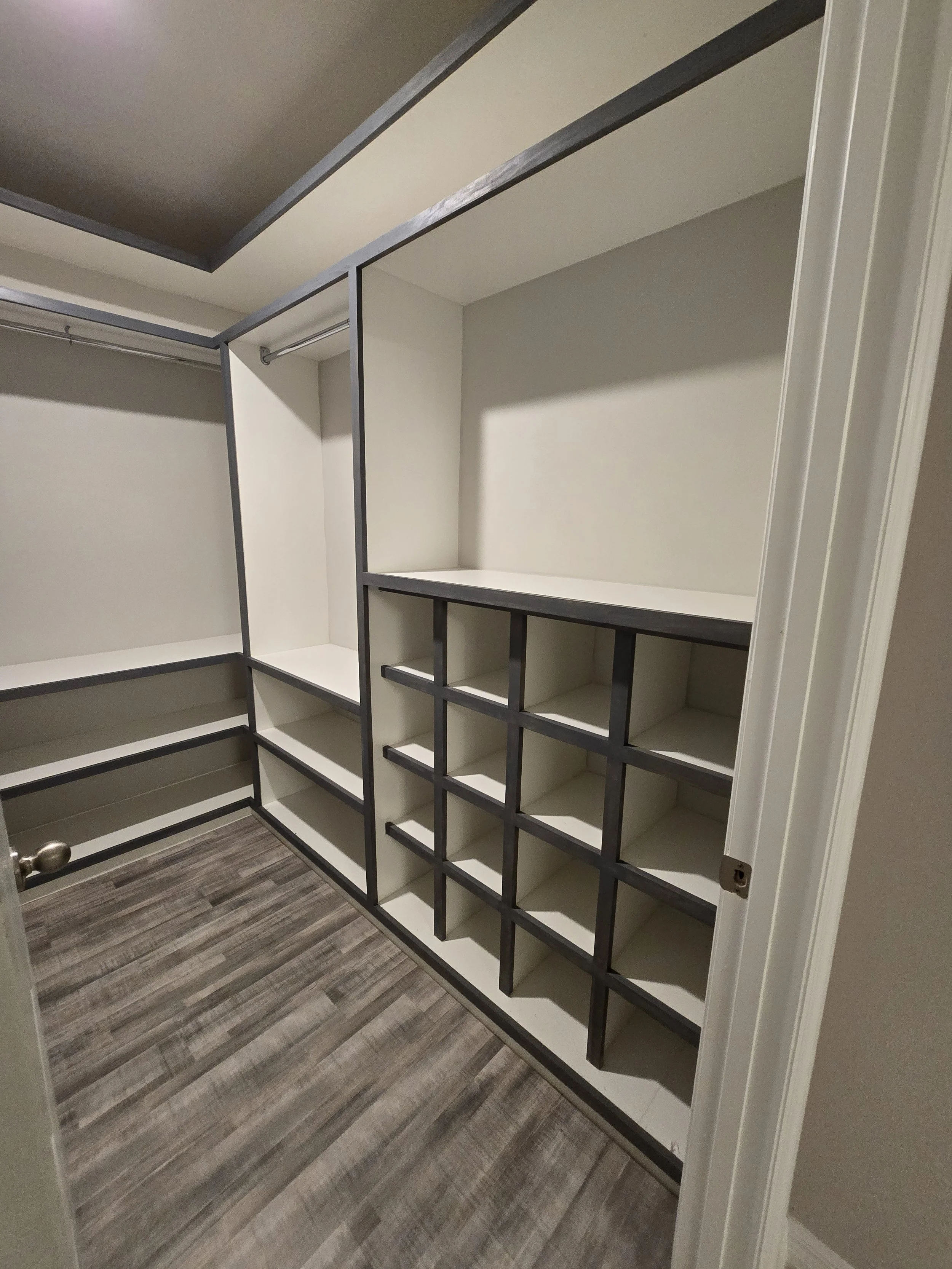 Empty walk-in closet with built-in shelving and hanging rods, wood flooring, and white walls.