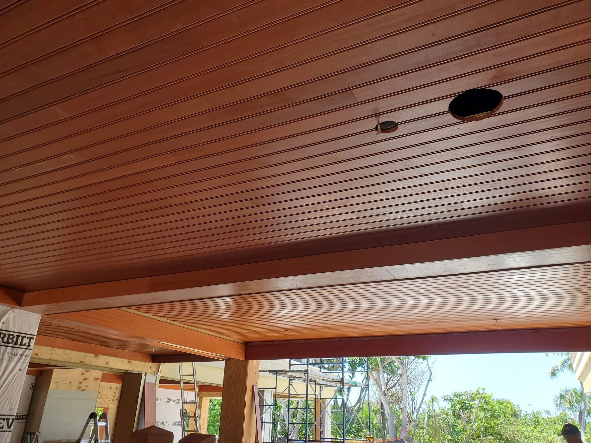 Wooden ceiling with two circular cutouts, one larger than the other, and construction materials and scaffolding visible in an outdoor construction site.