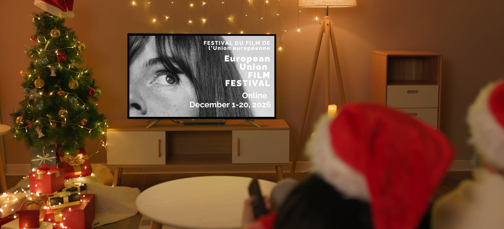 Living room decorated for Christmas with a Christmas tree, presents, and string lights. A TV screen displays information about the European Union Film Festival online event from December 1-20, 2026.