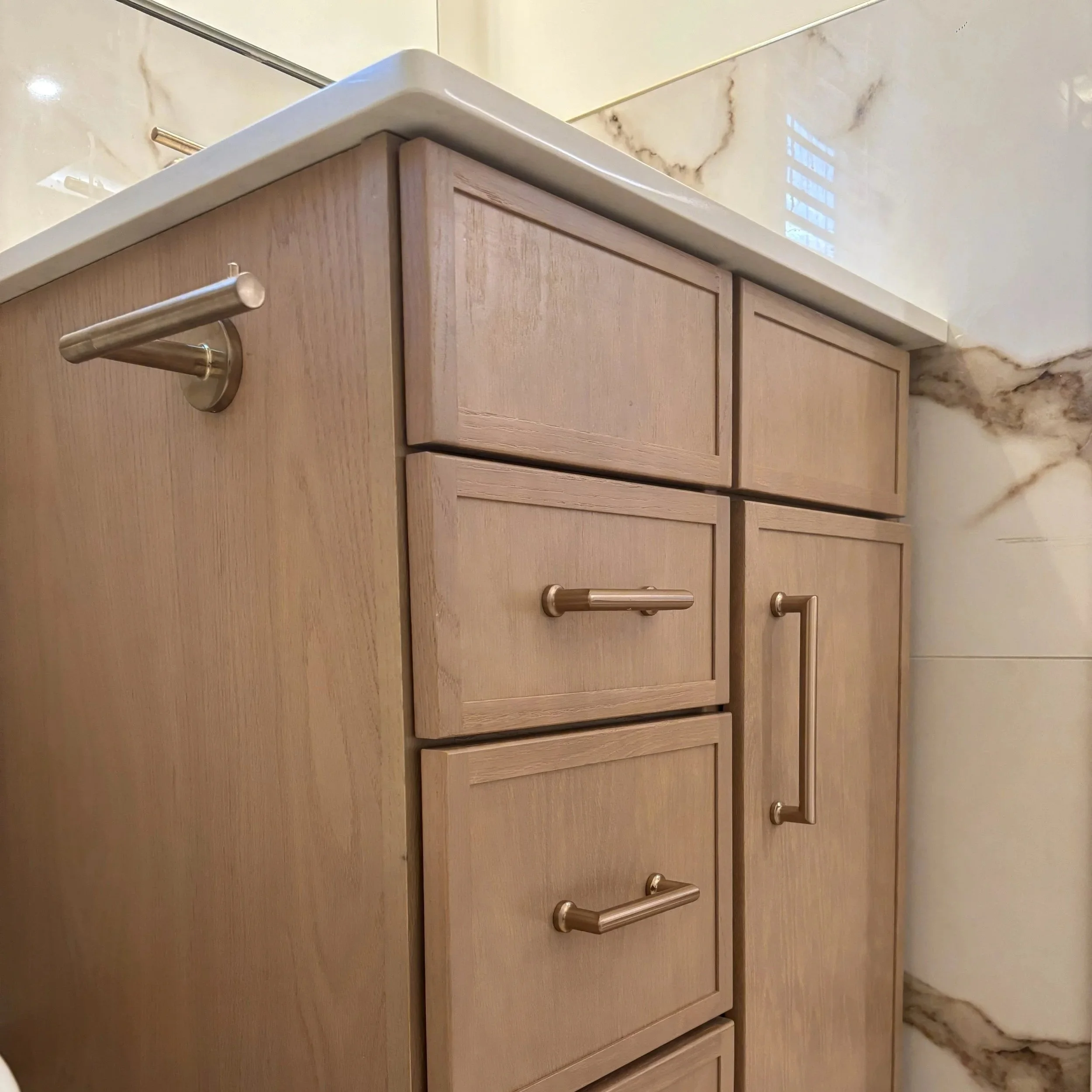 Close-up of a light wood cabinet with a metal handle, a marble countertop, and a wall with marble-like veining.