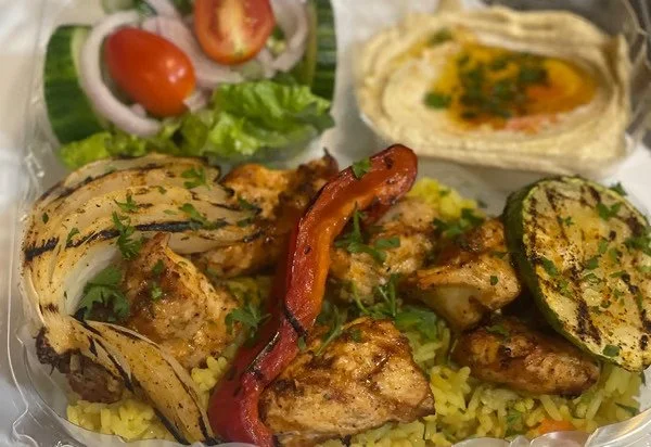 Plate of grilled chicken and vegetables with rice, side salad with tomato and onion, grilled zucchini, and a fried egg wrapped in a tortilla.