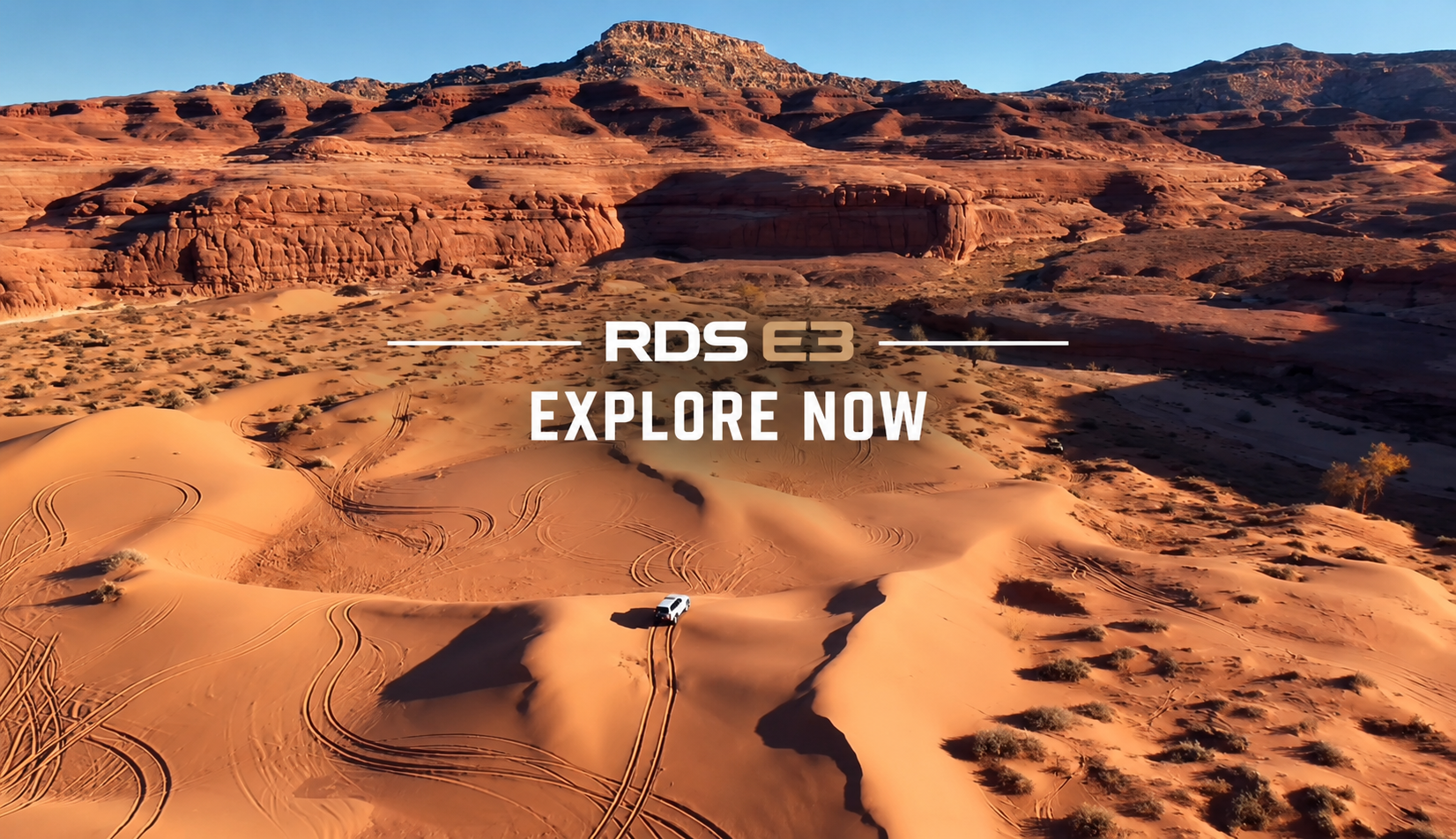 Desert landscape with sand dunes, rugged red rock formations, and a white off-road vehicle, promoting RDS E3 with the text "Explore Now."