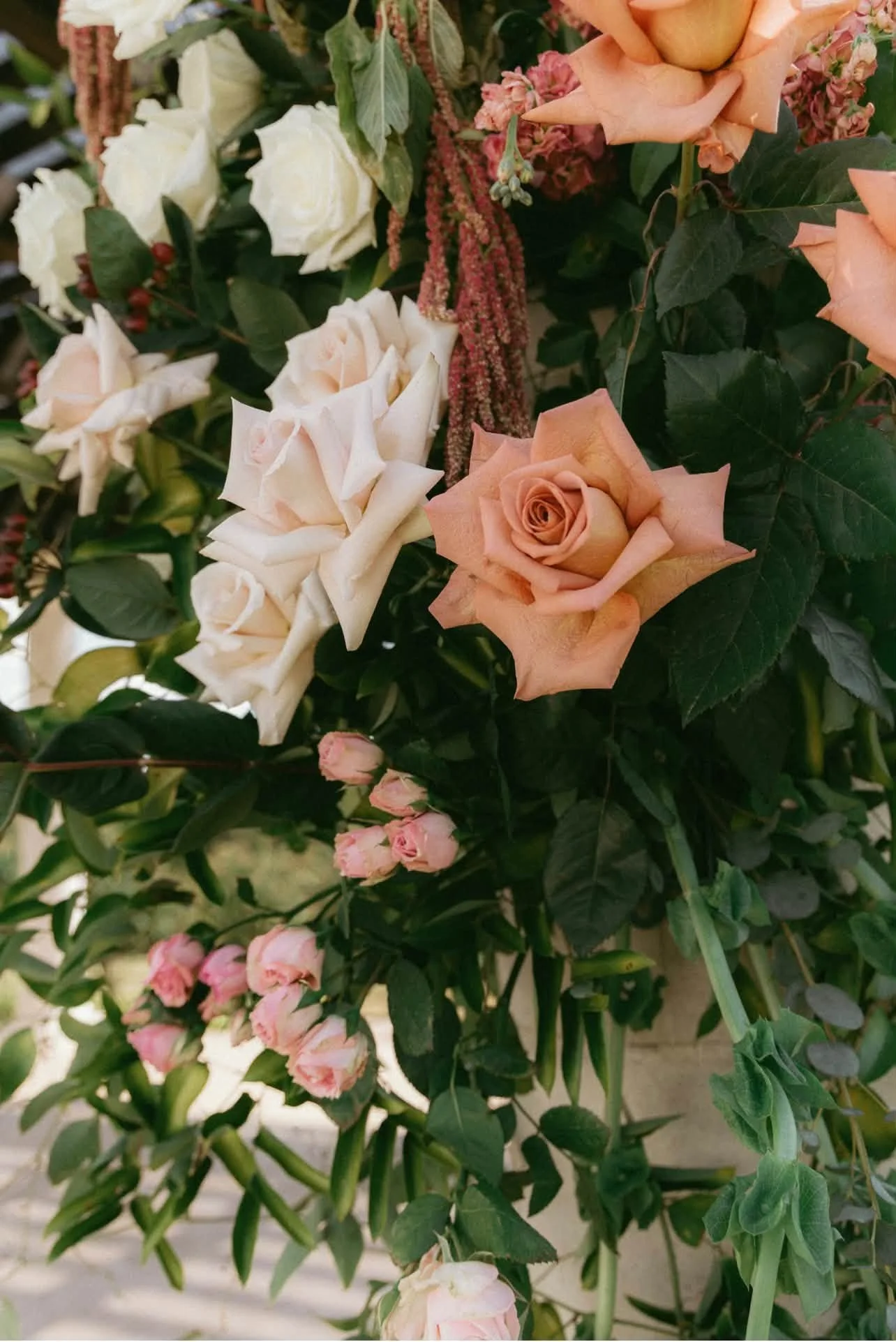 Close-up of a bouquet with peach and white roses, pink buds, and green leaves.