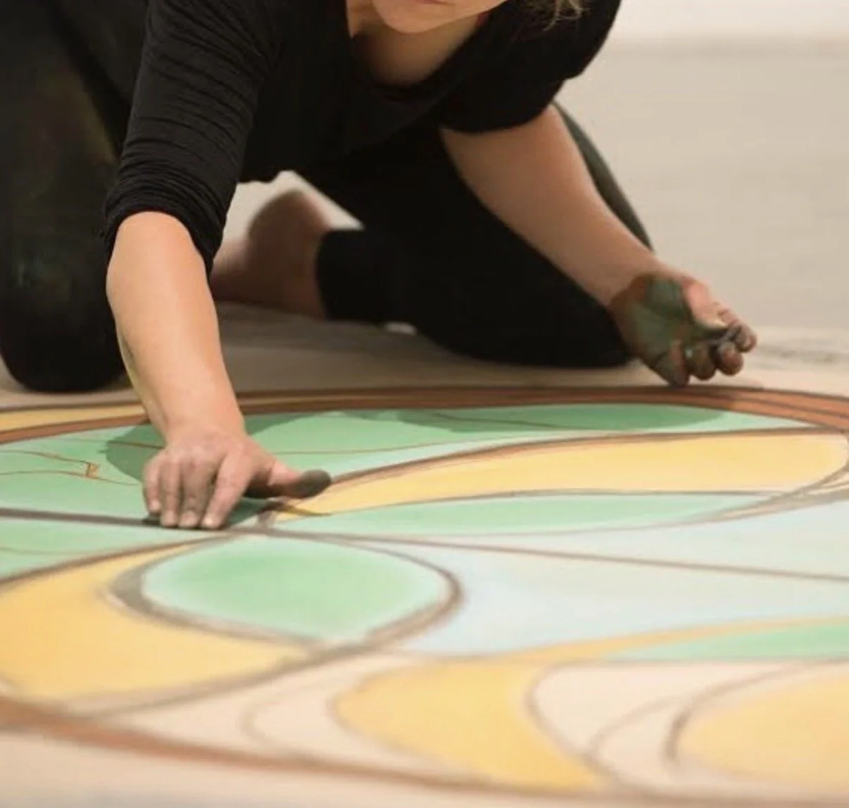 Person kneeling on the floor, working on a colorful artwork with hand-held tools.