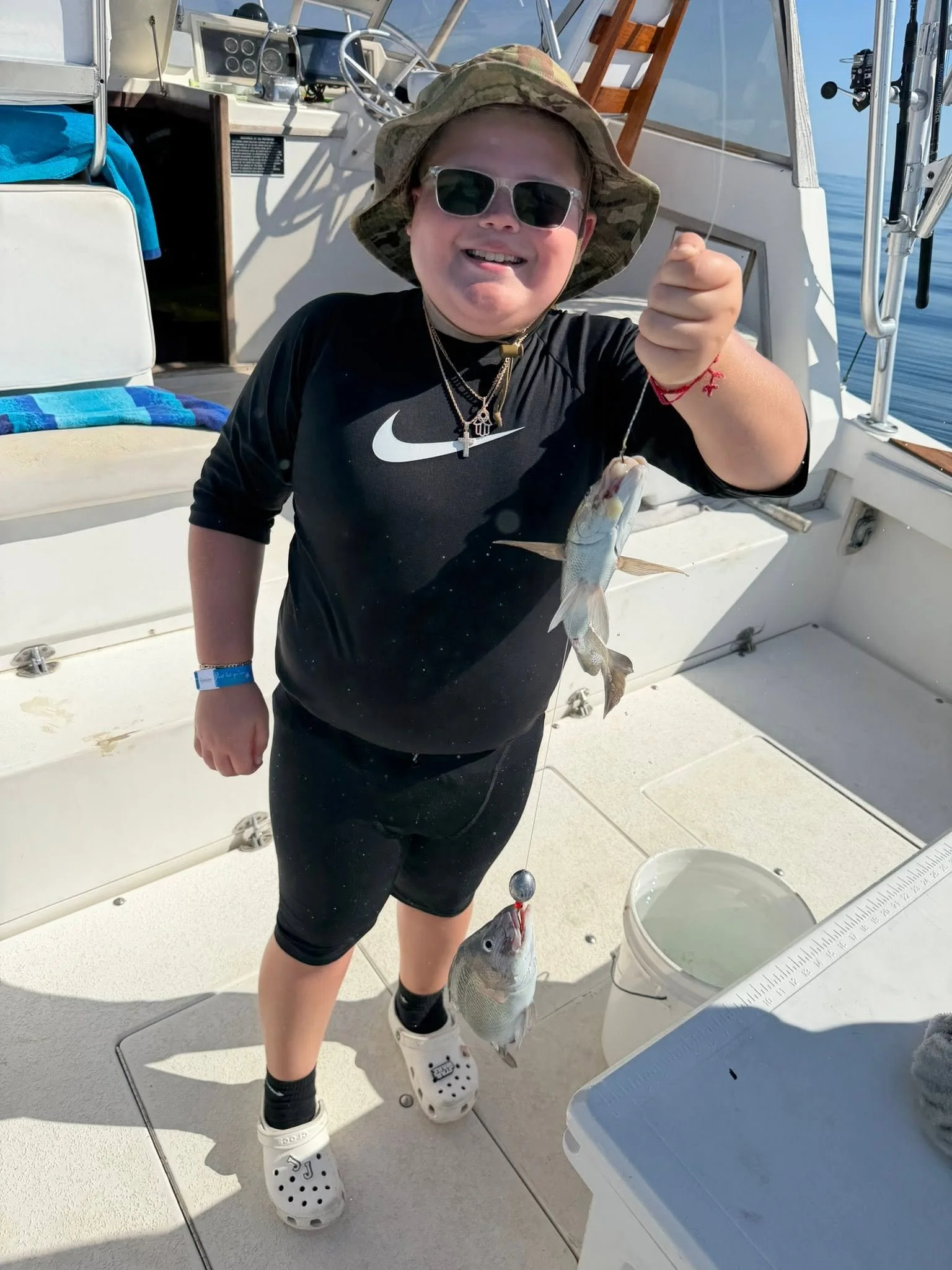 Young angler in a black shirt holding up a freshly caught fish aboard a charter fishing boat.