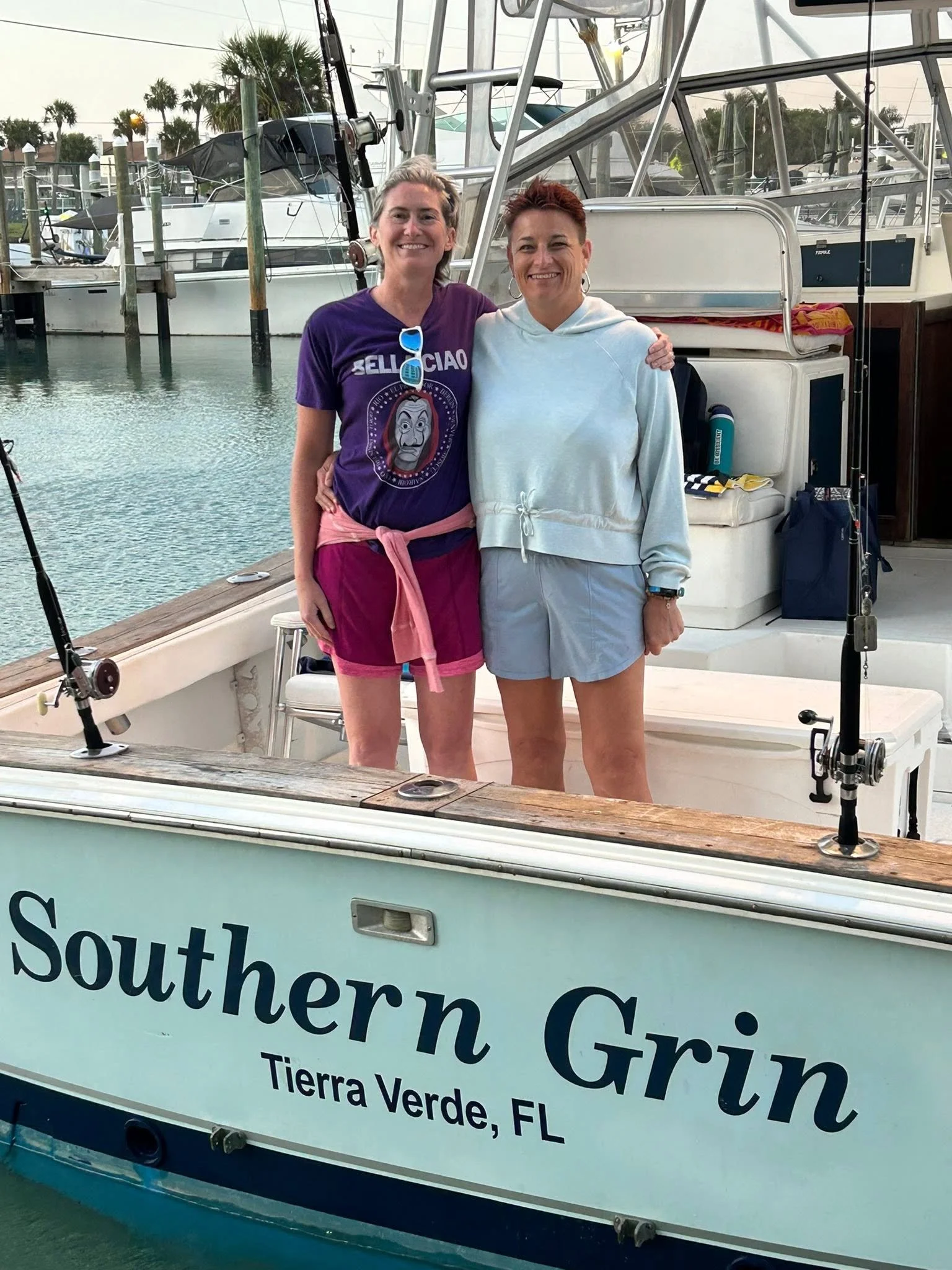 Two guests standing together on the deck of Southern Grin while the fishing boat is docked at a marina.
