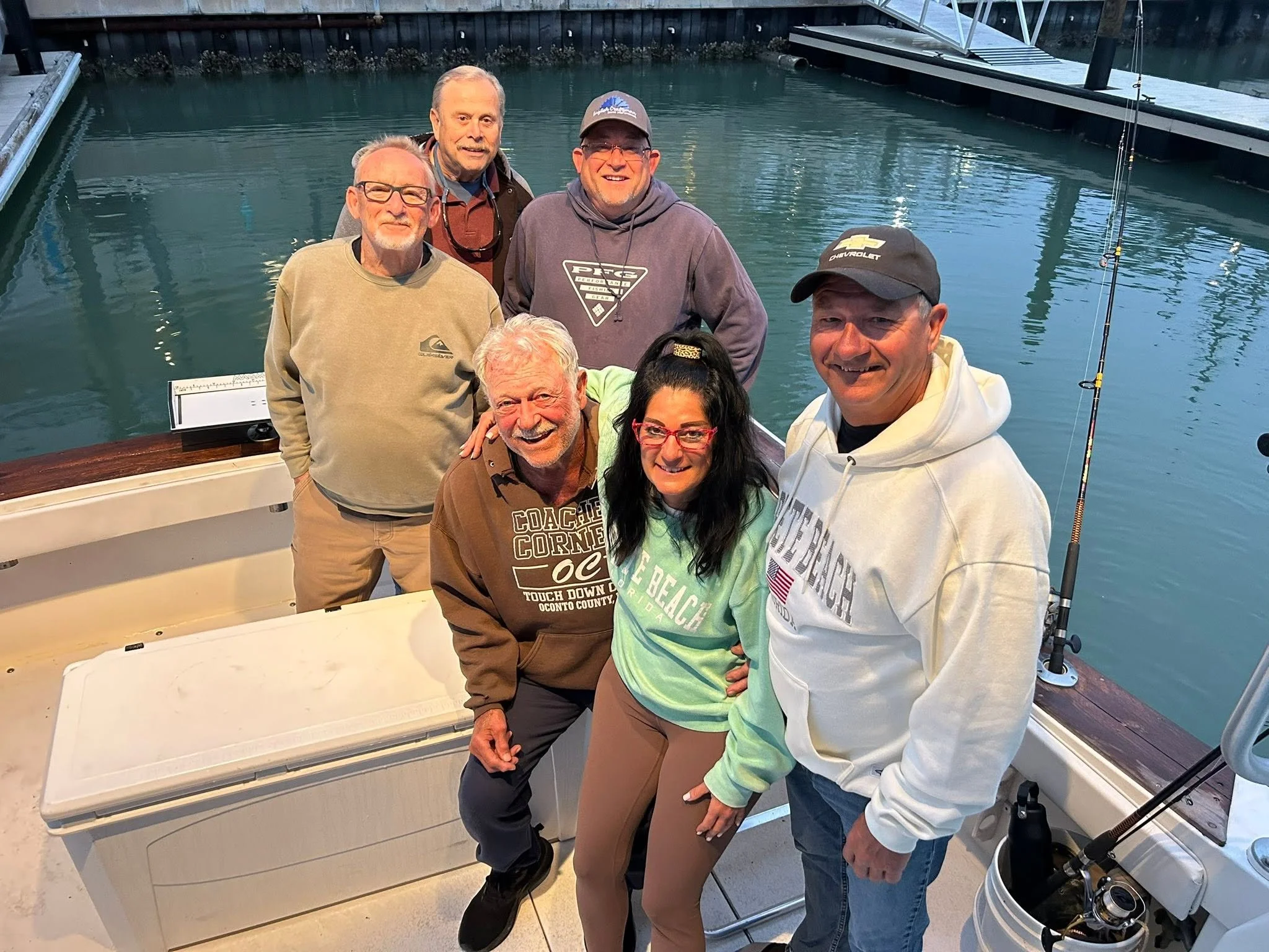 Group of six smiling guests posing together on the deck of a fishing charter boat at the marina.