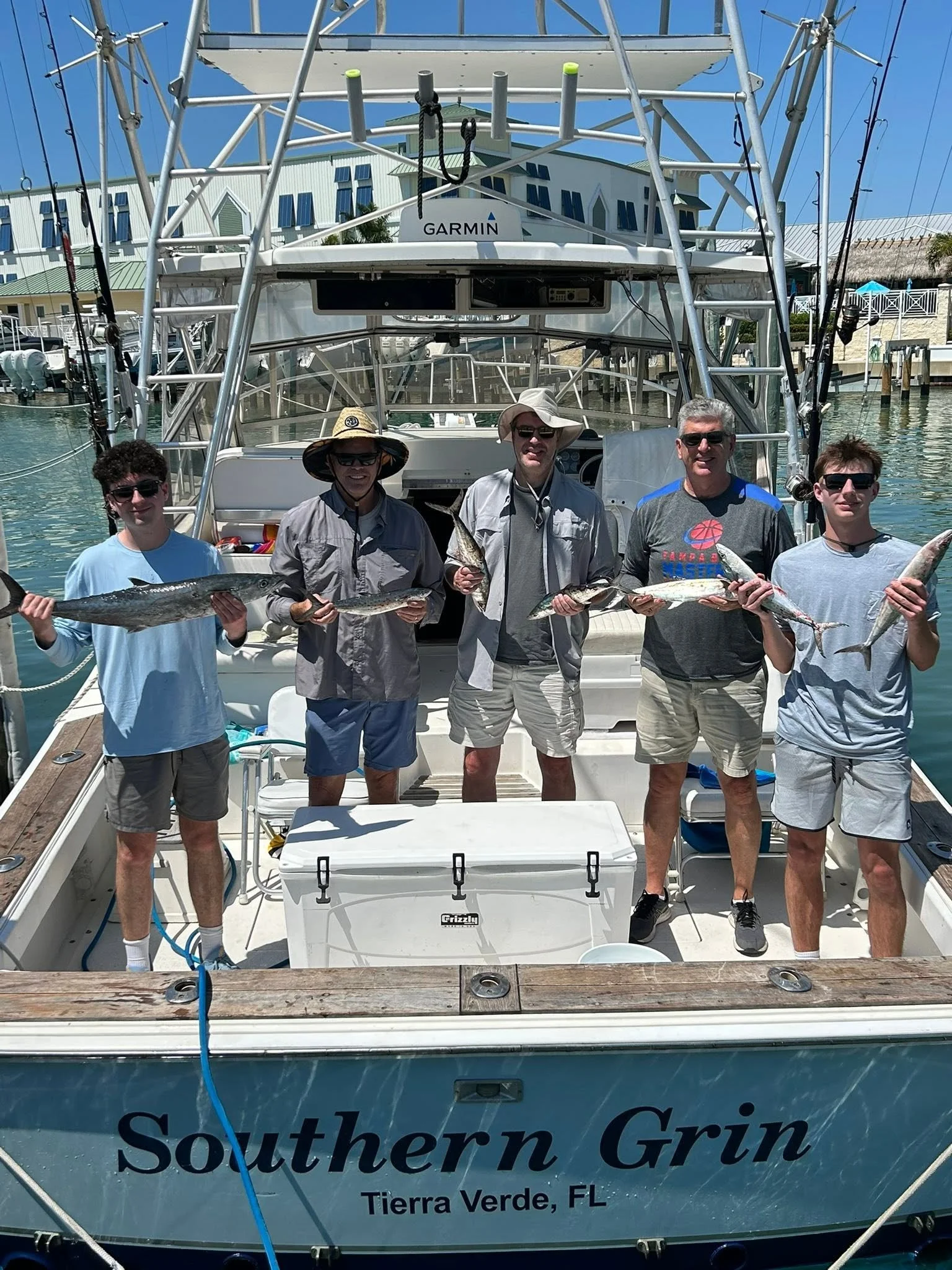 Five anglers standing aboard Southern Grin and displaying their freshly caught fish at the marina.