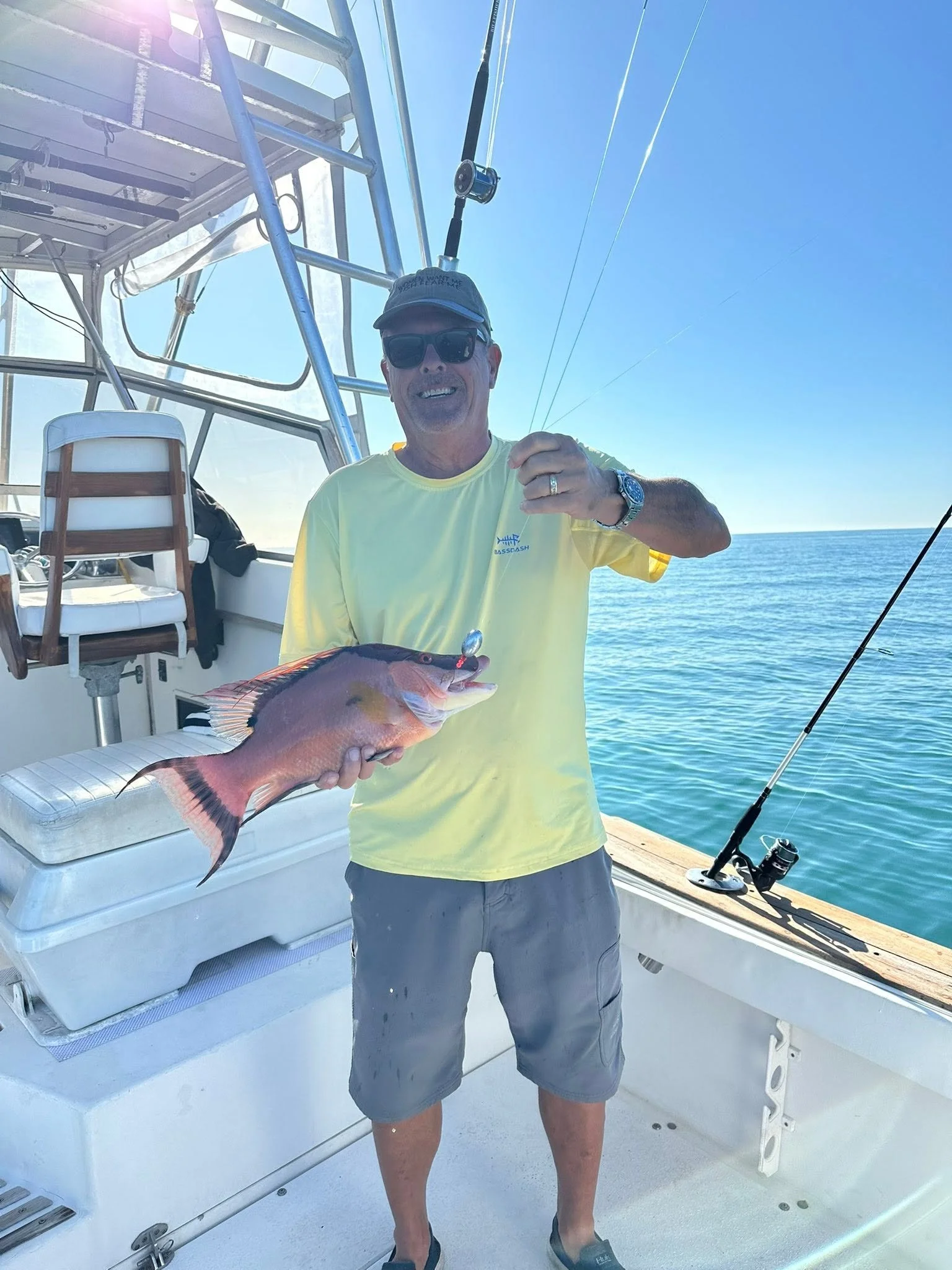 Smiling angler in a yellow shirt displaying a colorful pink fish aboard a fishing charter boat on the Gulf.