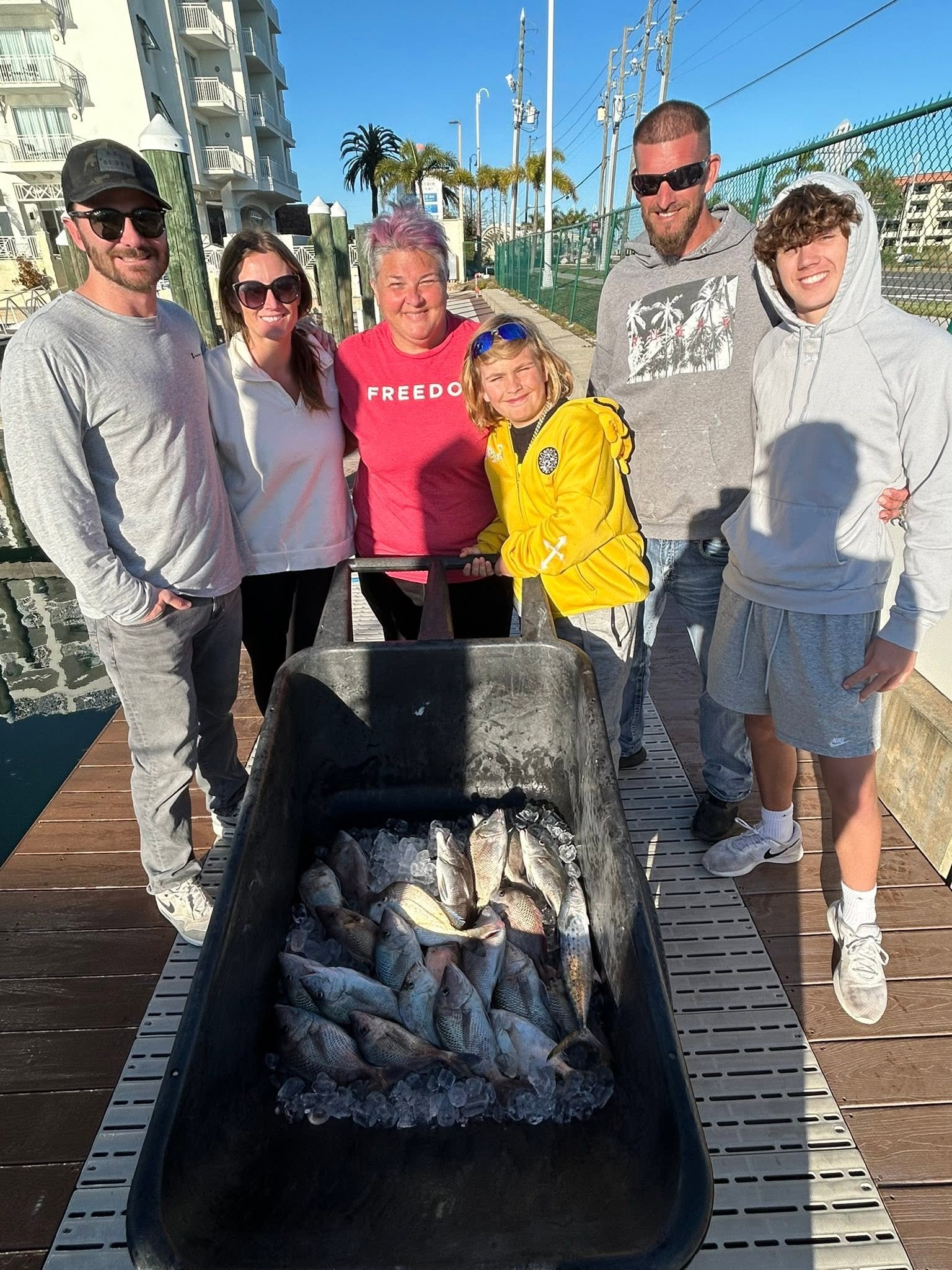 Group of five anglers standing beside a cart filled with freshly caught fish after a fishing trip.