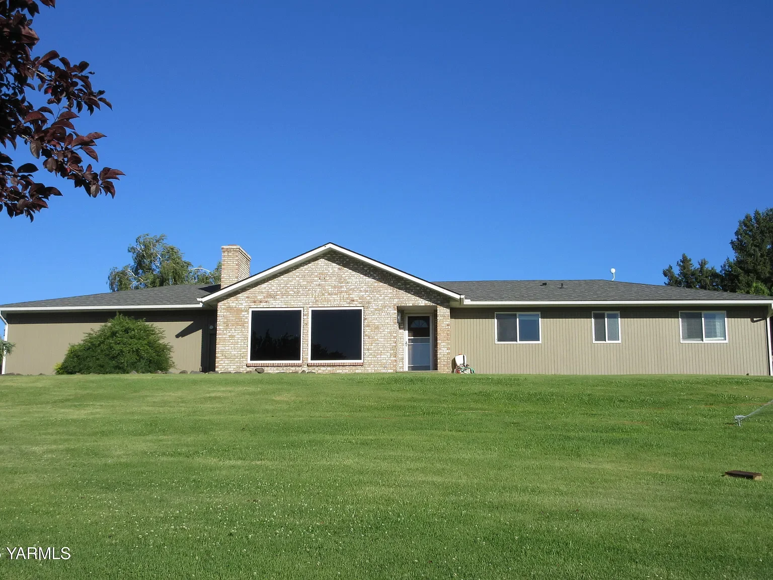 Single-story house with brick and siding exterior, large front yard, and clear blue sky.