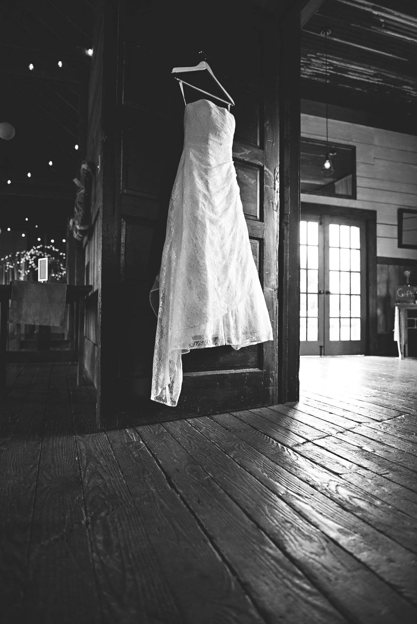 A wedding dress hanging on a wooden door in a rustic venue, with wooden floorboards and a large window in the background.