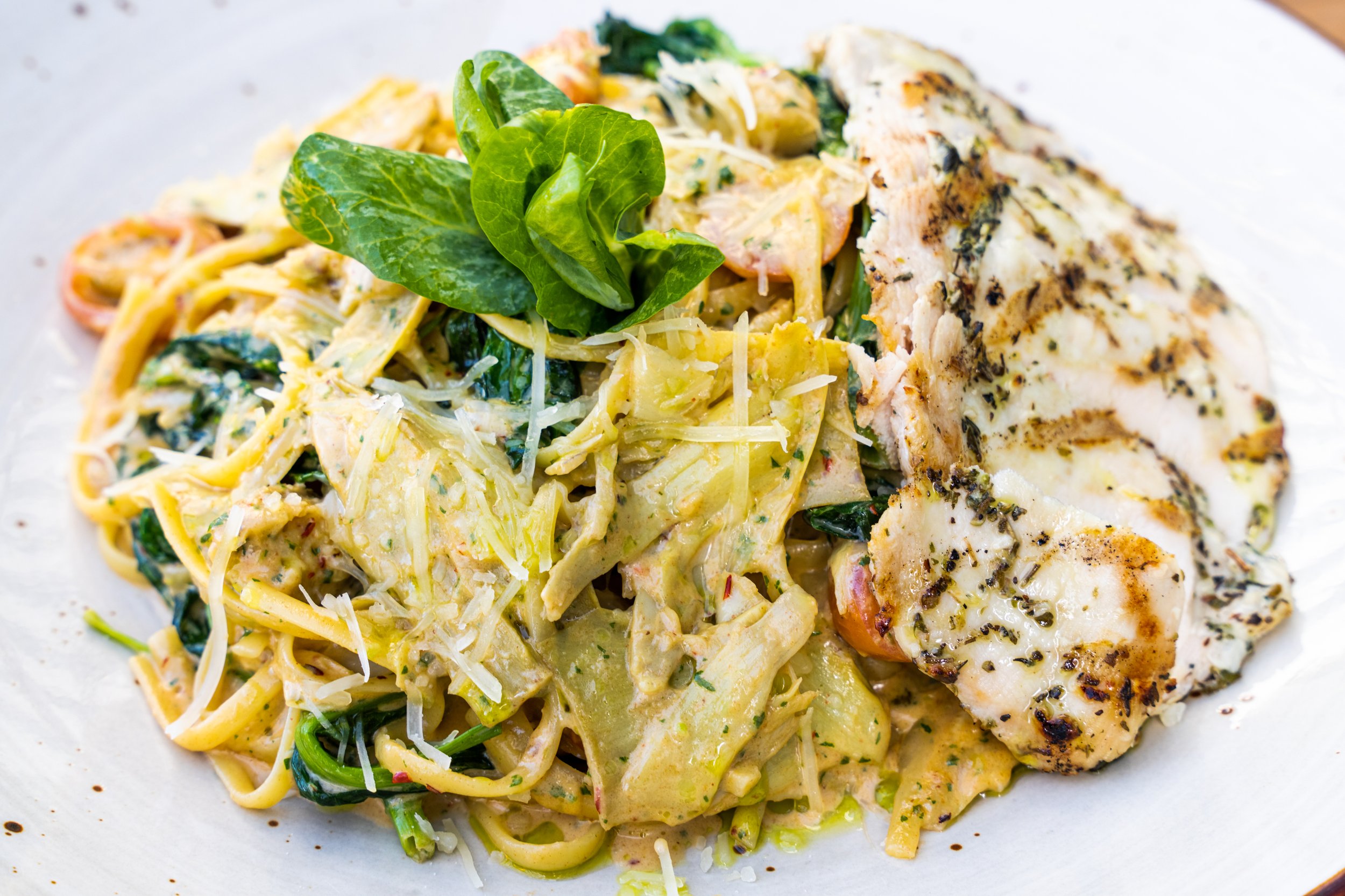 Close-up of a plate of pasta with grilled chicken, topped with fresh basil and shredded cheese.