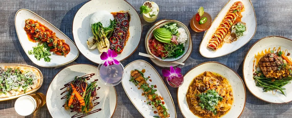 Variety of Japanese sushi and dishes on a gray wooden table, with colorful garnishes and drinks.