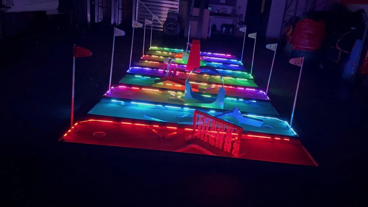 Miniature golf course with colorful lights and flags, viewed at night.