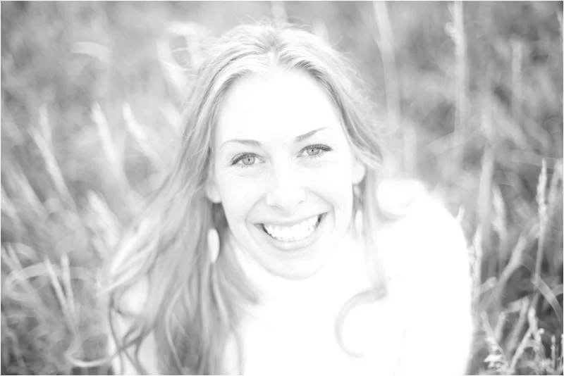 A woman smiling outdoors in a field of tall grass.
