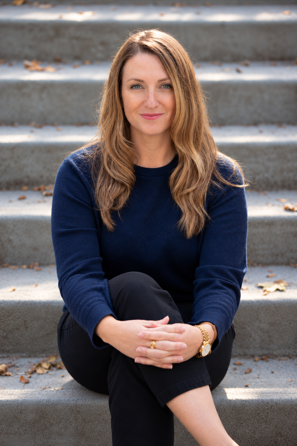 Kristine Burkman, PhD, clinical psychologist, seated on outdoor steps and smiling at the camera.