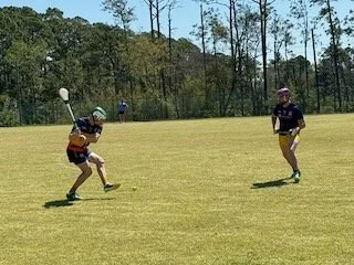 Two children playing flag football on a grassy field with trees in the background.