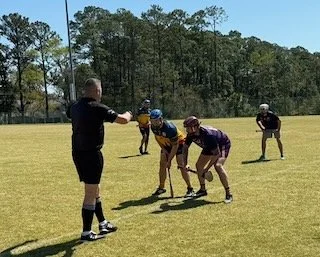 Football coach instructing players on a grassy field, with trees in the background.