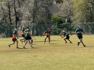Youth football game with players running on the field, some wearing helmets and jerseys, during daytime.
