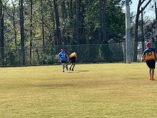 Two football players on a field competing for the ball, with a third player nearby.
