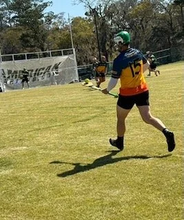 A person playing ultimate frisbee on a grassy field, wearing a green helmet, a blue, yellow, and red jersey with the number 12, black shorts, and black shoes.