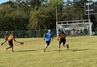 Two people playing hockey on a grassy field with a goalpost and a banner in the background.