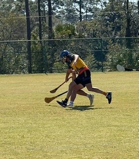 Two young children playing hockey on a grassy field during daytime.