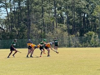 A group of people playing flag football on a grassy field with a wooded background.