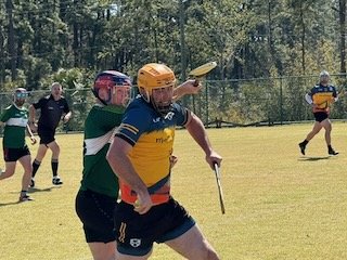 Two players in a sports game, wearing helmets and jerseys, competing on a grassy field with others in the background.