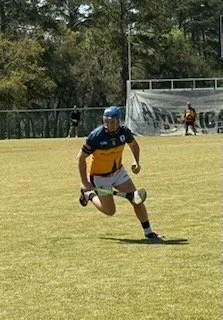 A person in a blue helmet and sports gear running on a grassy field during a game
