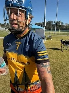 A male athlete in a blue and yellow sports jersey with the number 7, wearing a blue helmet, standing outdoors on a sports field, with a water bottle visible.