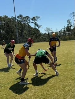 Children playing a game outdoors on a grassy field, wearing helmets and sports gear.