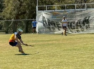 Child with helmet crouching and holding a stick on a grassy field during a sports game.