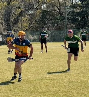 Hockey players on a grassy field, preparing for play, with spectators in the background.