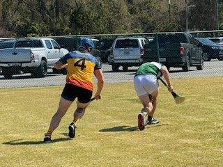 Two football players on a grassy field, one in a yellow and black jersey with the number 4, and the other in a green shirt and white shorts, running.