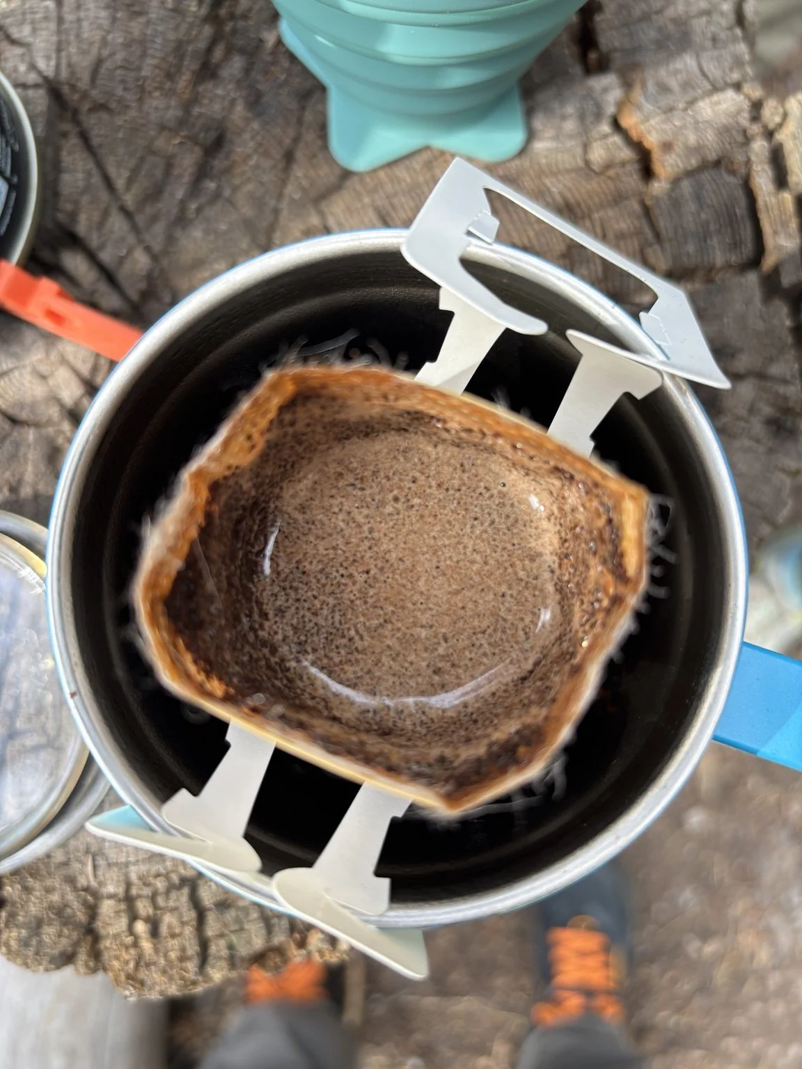 A portable camping coffee maker with brewed coffee inside, placed on a wooden surface outdoors.