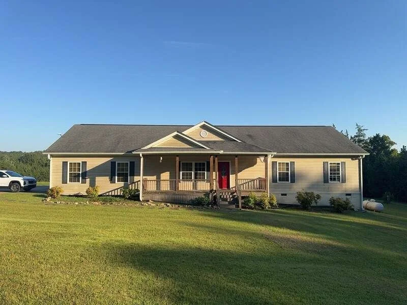Tan home with a broad shingle roof, front porch, and lawn
