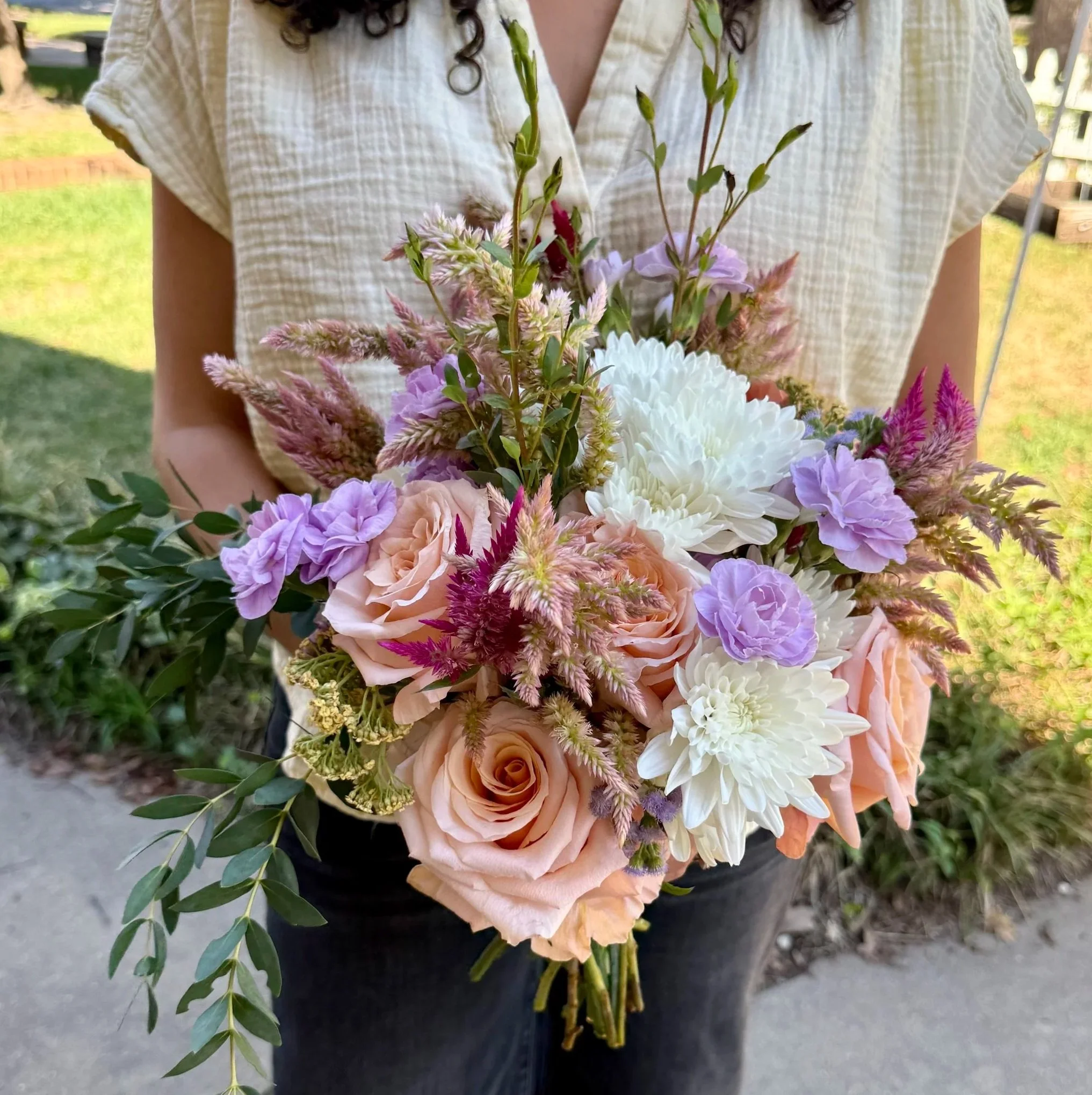 Person holding a colorful bouquet of mixed flowers outside on a sunny day.