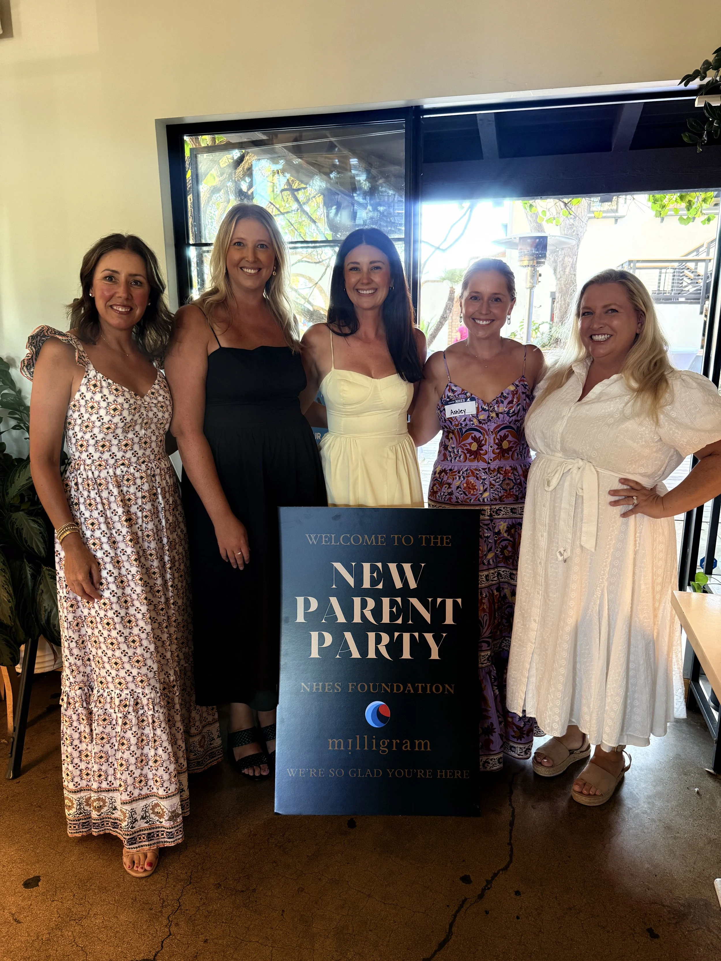 Five community members gathered behind the NHES Foundation New Parent Party welcome sign.