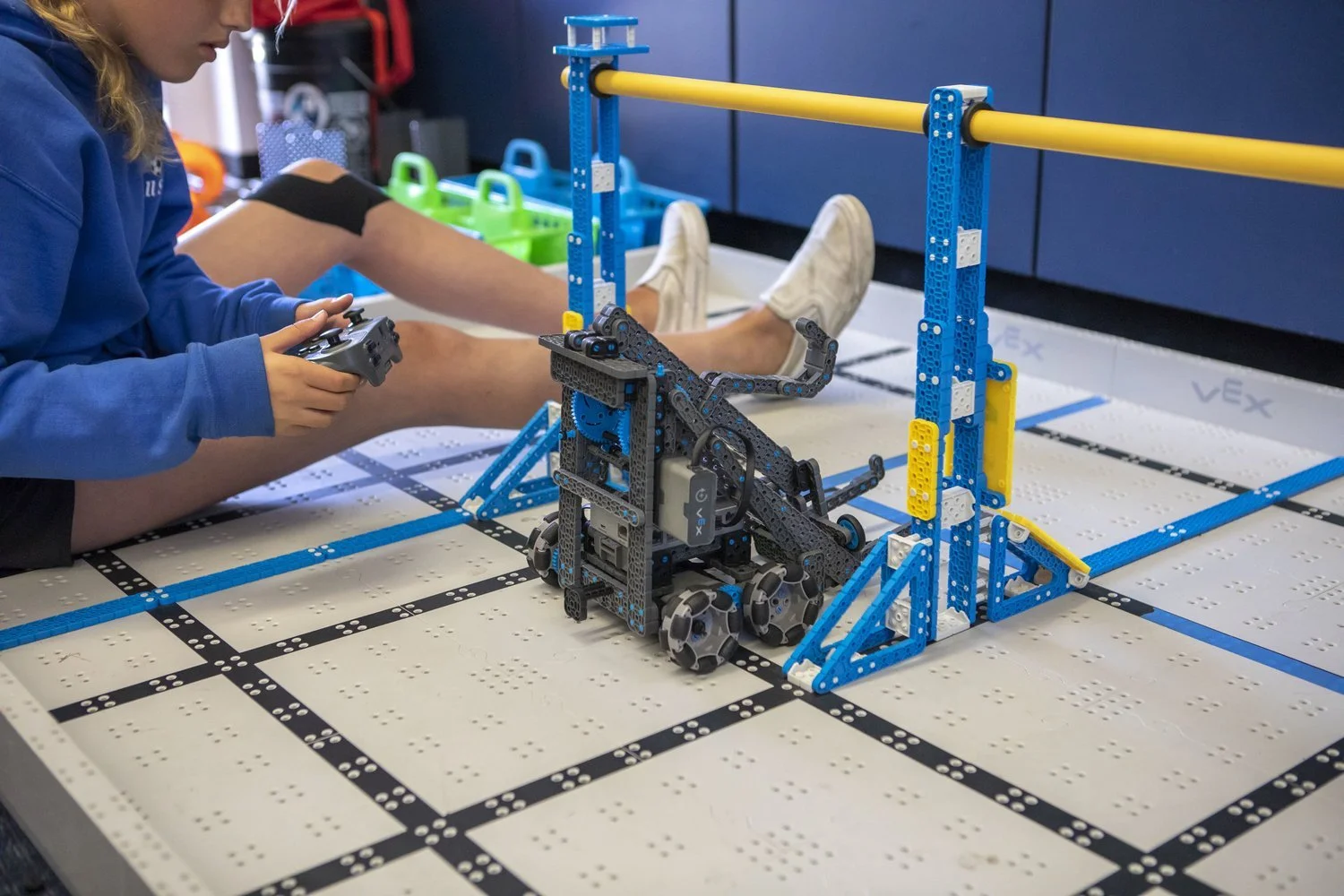 A VEX IQ robot on a marked robotics field beside blue and yellow structures.