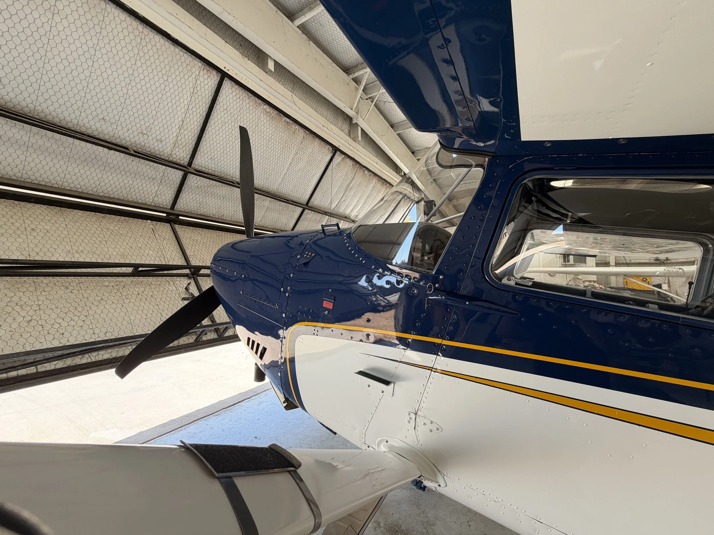 Close-up of a blue helicopter's cockpit and nose, situated inside a hangar with white insulation panels and metal framework.
