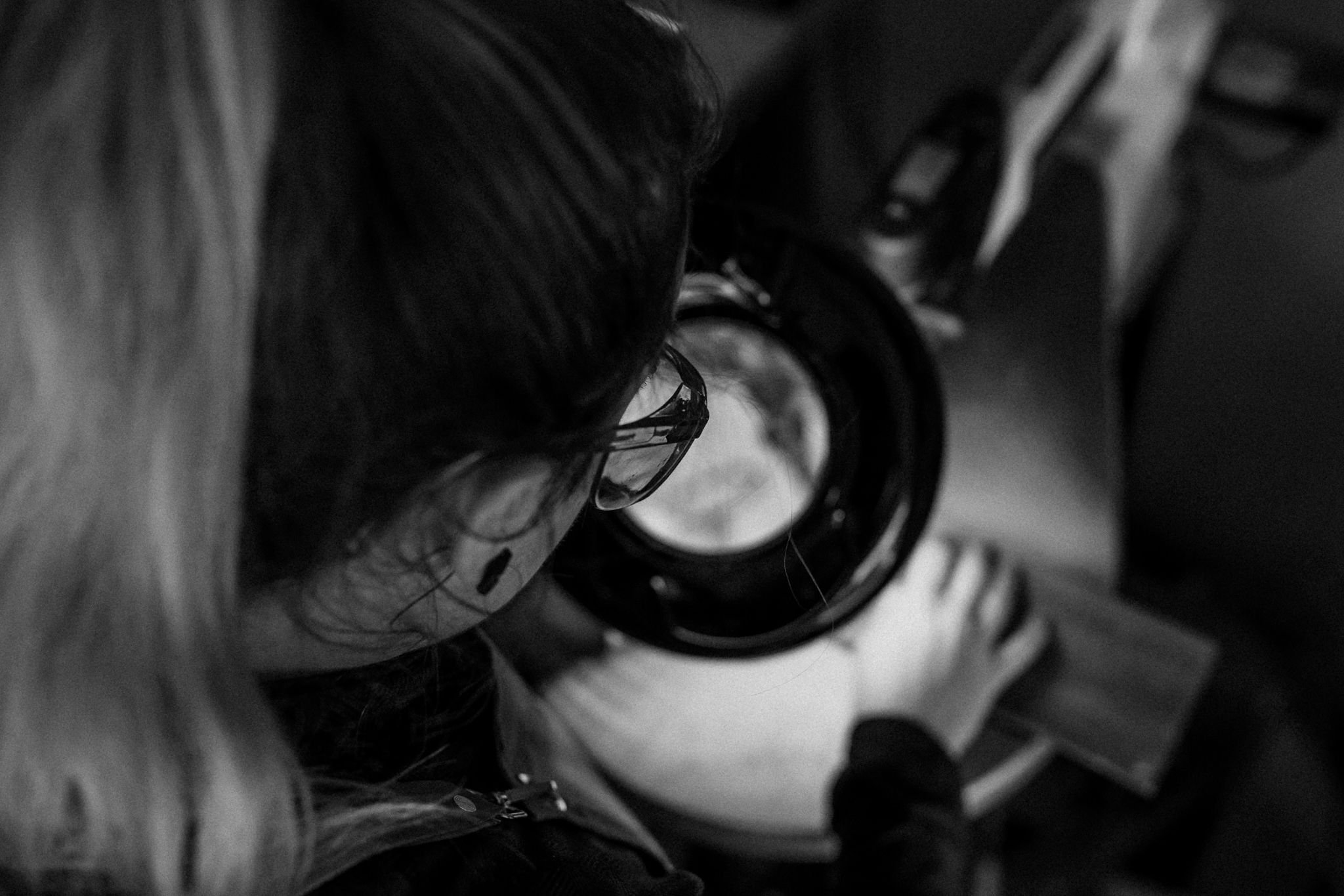 Close-up black and white photo showing multiple pairs of glasses placed on a surface, with a focus on the frames and lenses.