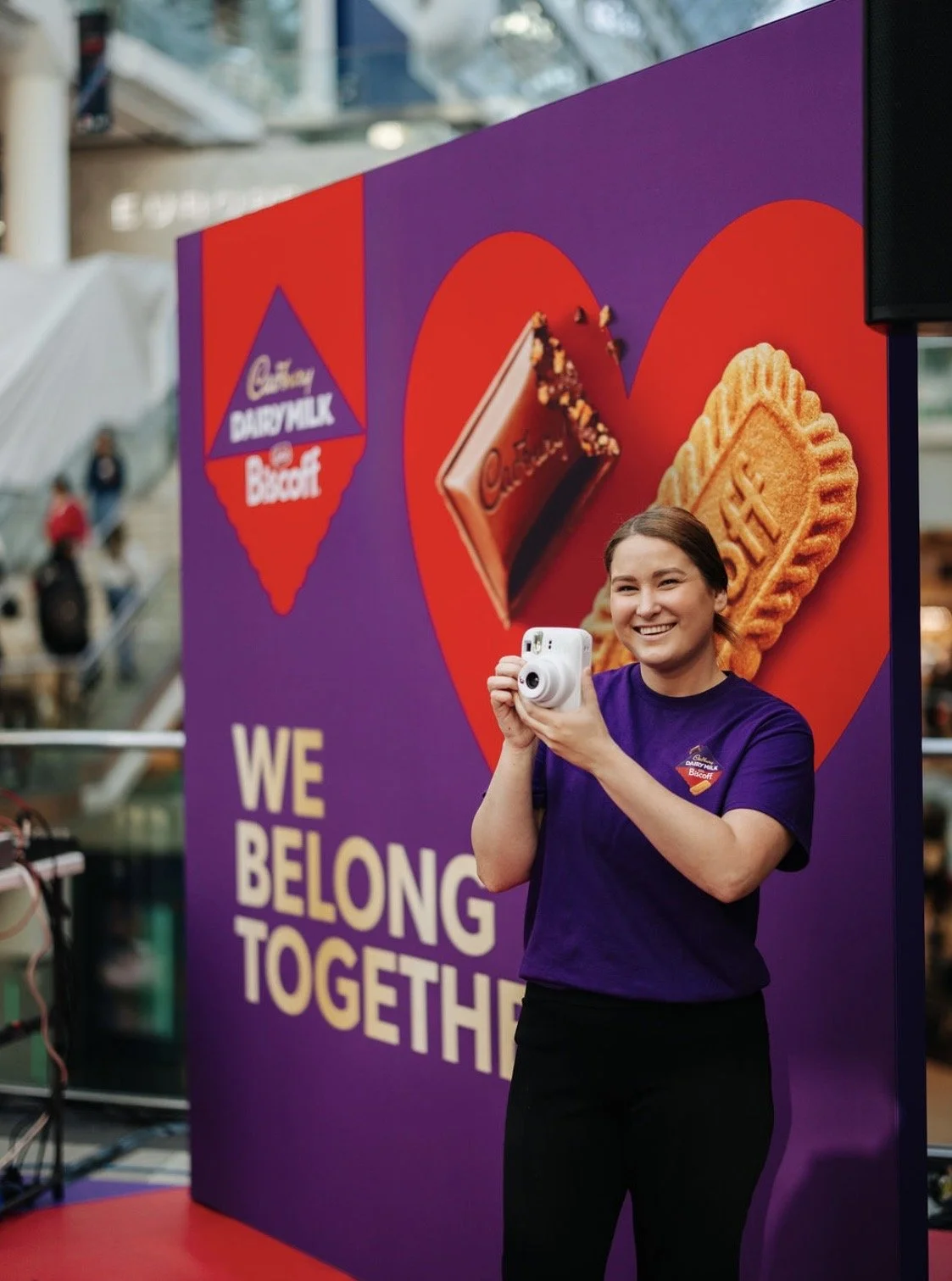 Smiling woman holding a white instant camera at a Cadbury Dairy Milk Biscoff promotional display in downtown Toronto