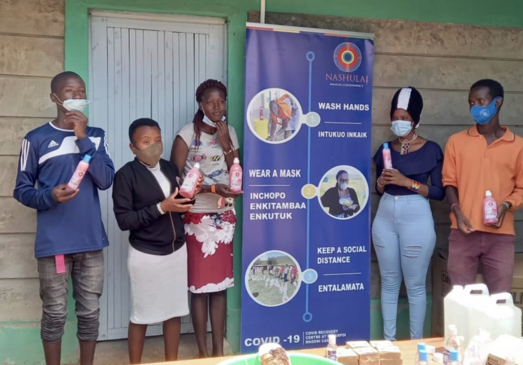 Five masked people holding hand sanitizer beside a COVID-19 prevention sign