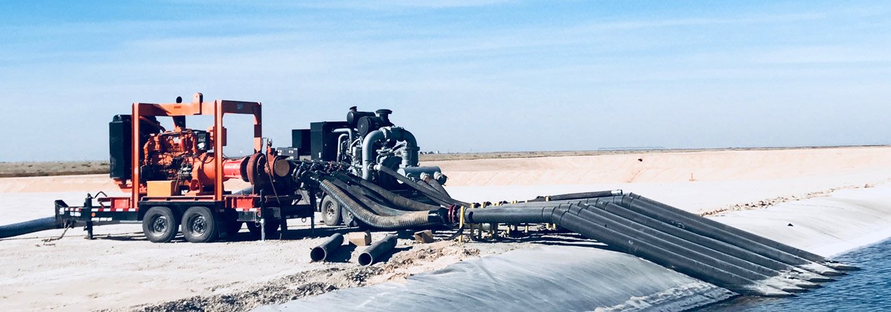 Trailer mounted high pressure pump feeding poly pipe into a lined frac water pit