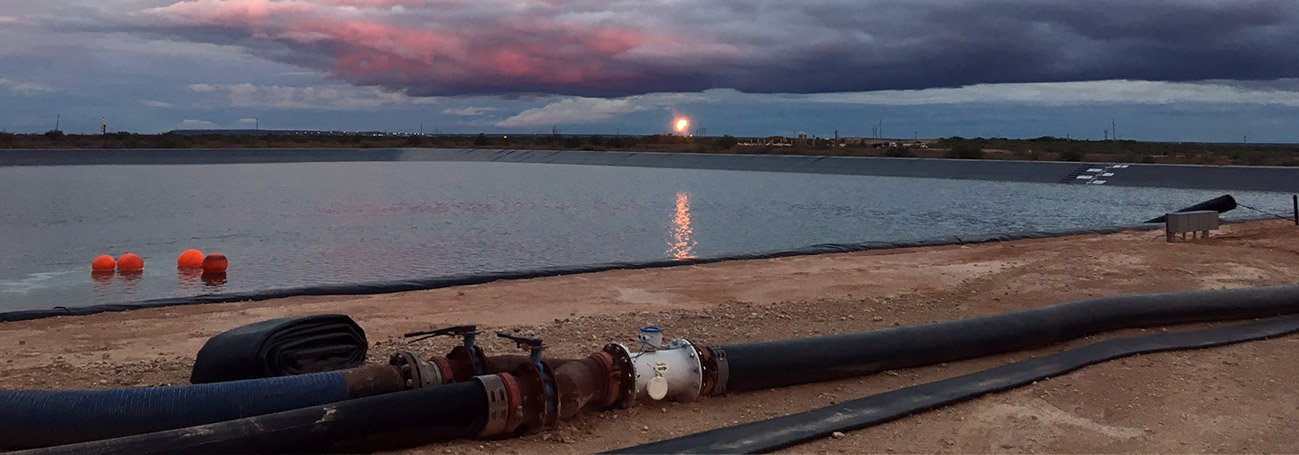 Qwik Pipe layflat hose line running to a frac water pit at sunset in Texas