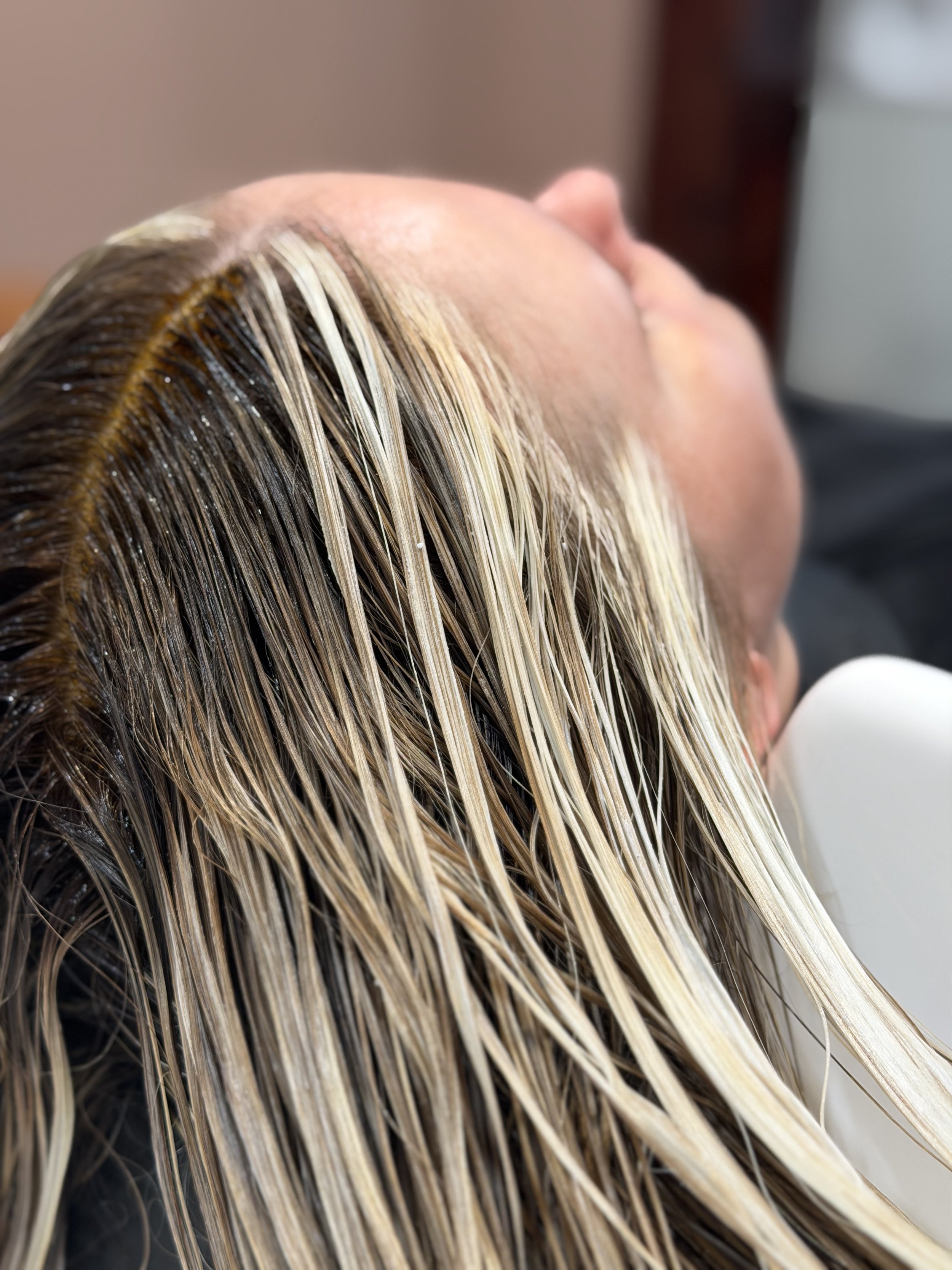 Close-up of a person's hair being processed with hair dye or toner, showing wet, blonde hair strands.
