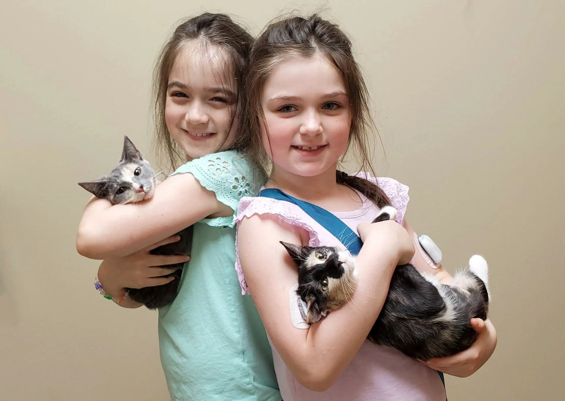Two smiling girls standing back to back, each holding a kitten