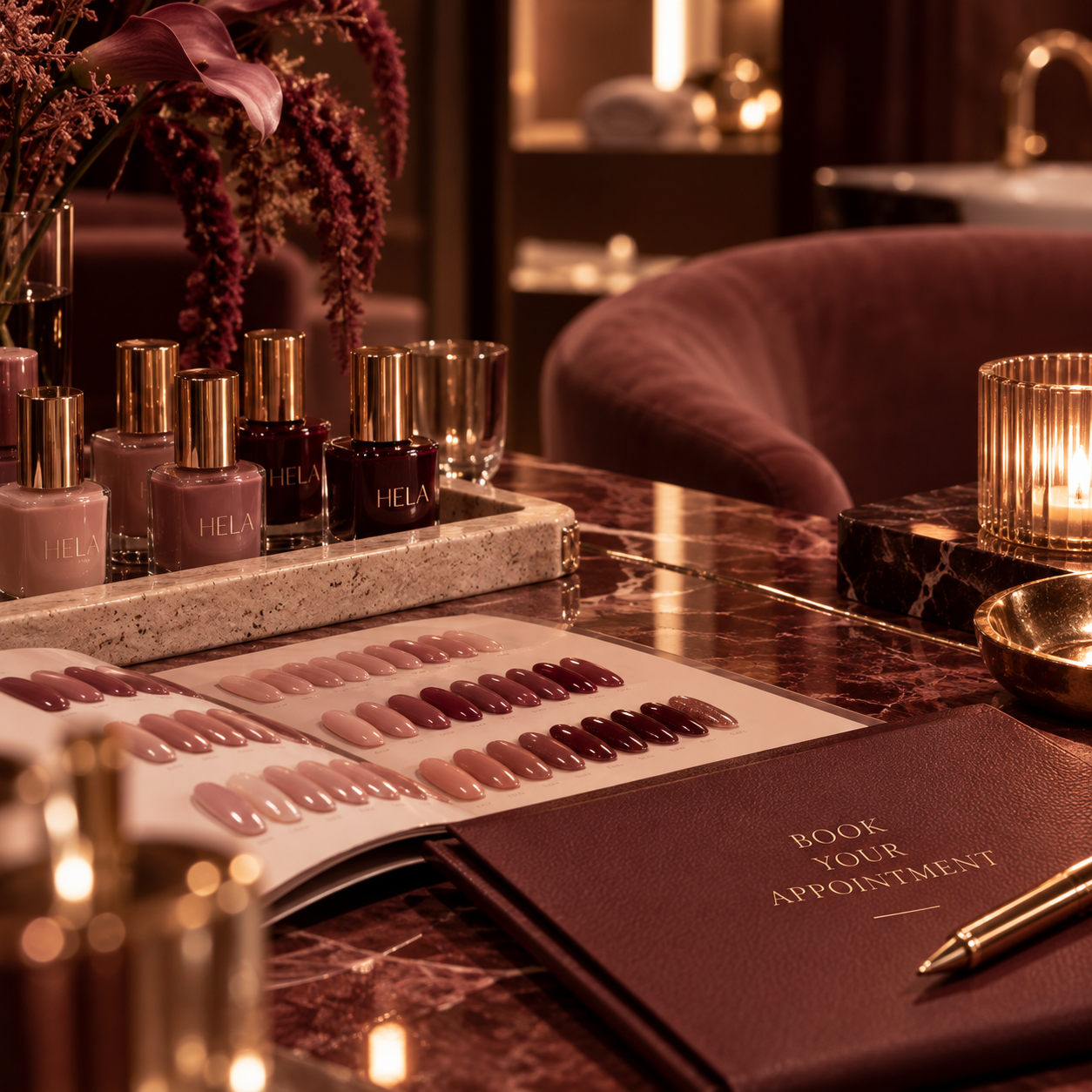 A manicure station with nail polish bottles, a nail color swatch, a book titled 'Book Your Appointment,' and a lit candle on a marble table in a cozy, dimly lit setting.